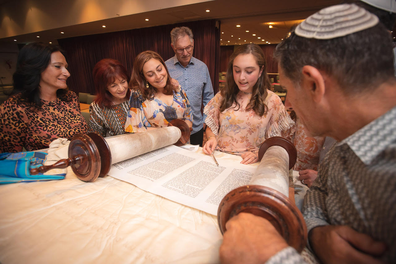 Bat mitzvah student reading from the Torah with family at Shira